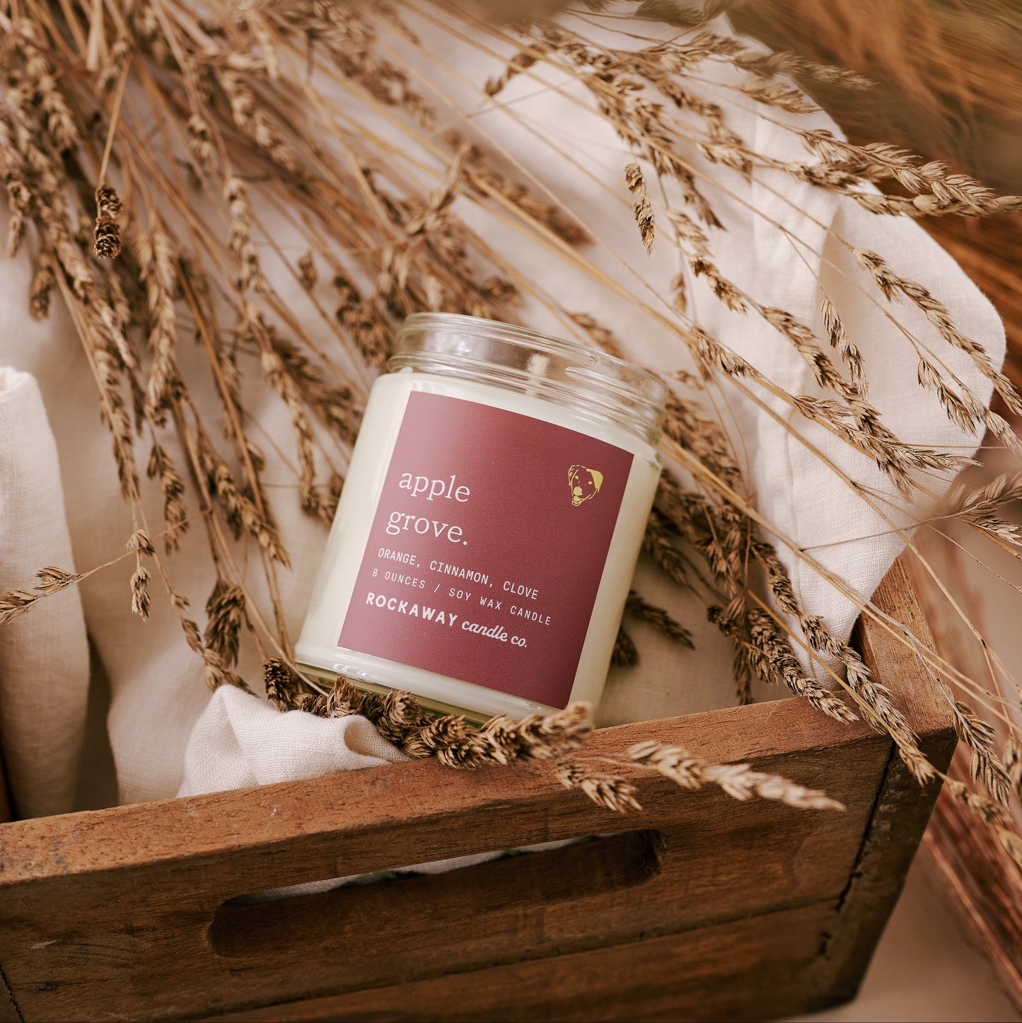 Candle labeled 'Apple Grove' in a wooden crate with decorative straw and fabric