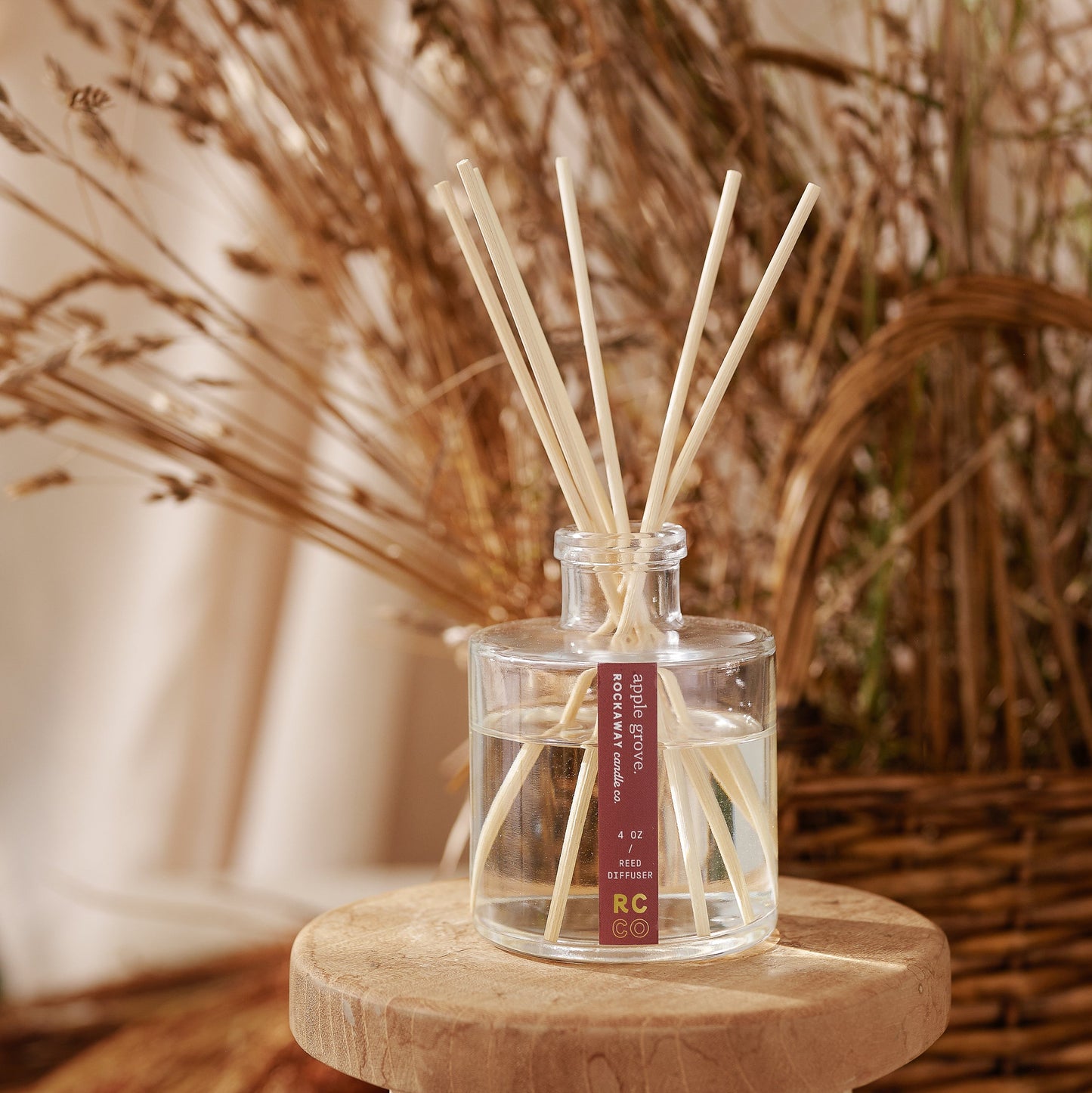 Glass diffuser bottle with reeds on a wooden stool against a natural background