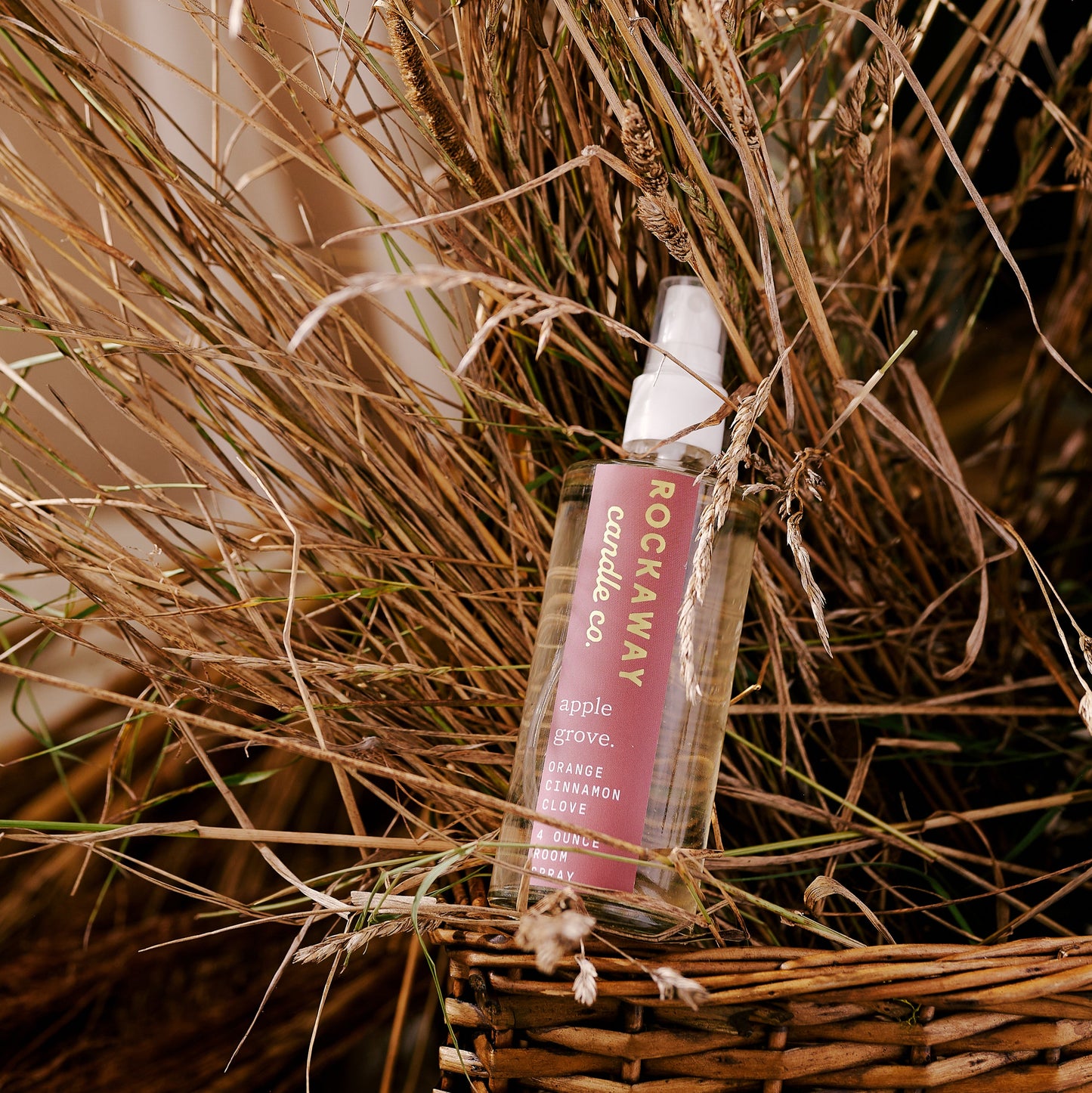 Spray bottle with pink label on a woven basket with dried grasses